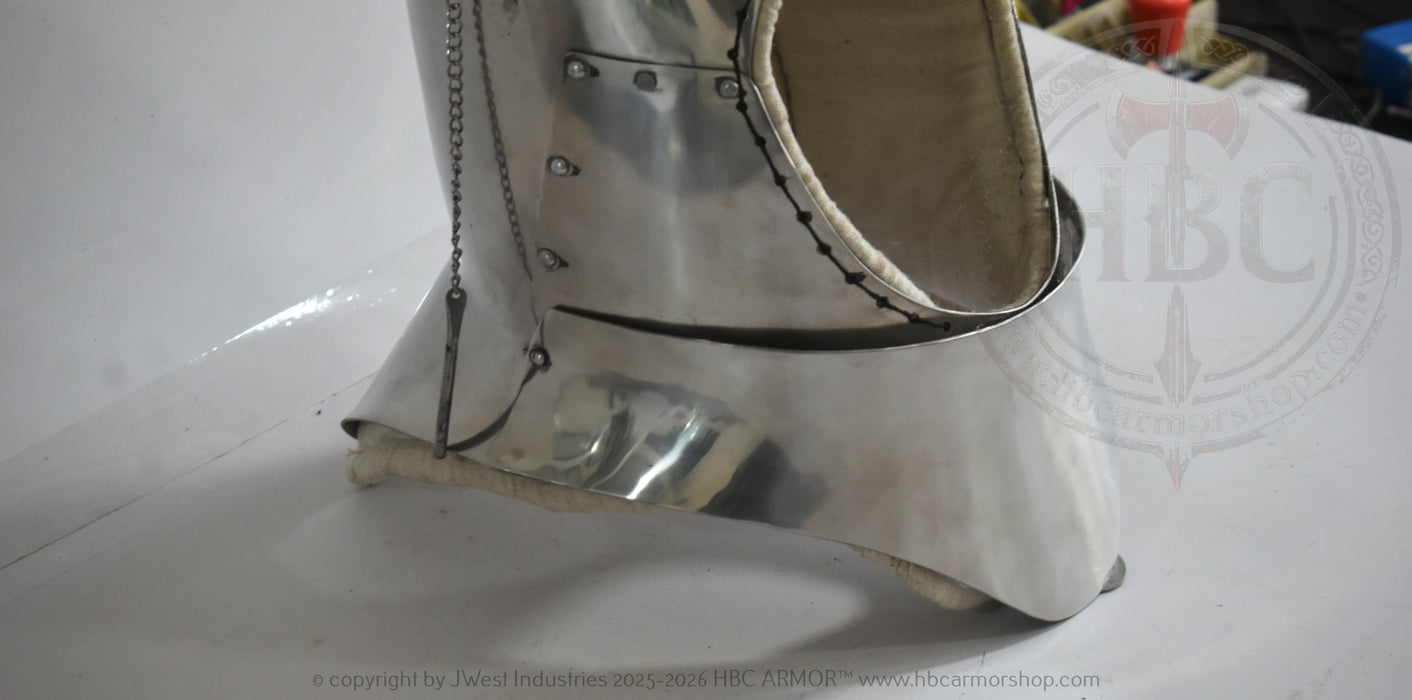 A close-up of a metallic silver medieval-style boot or boot cover with rivets and a chain detail, photographed on a white surface.