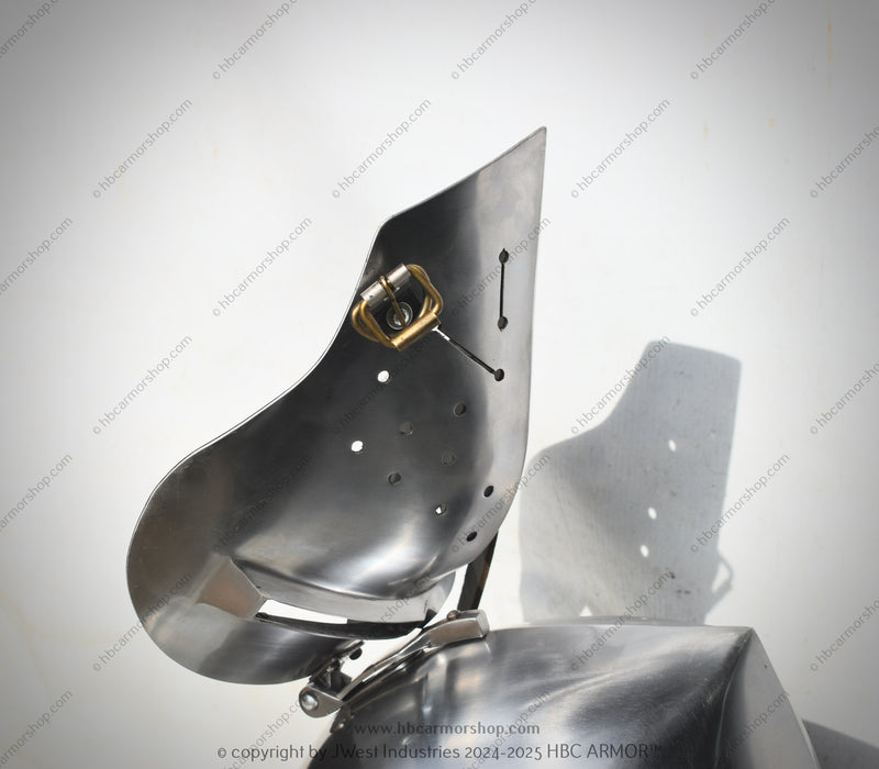 A close-up of a metallic armor plate or shield component with a polished steel finish, featuring pre-drilled holes and a small brass-colored hardware detail, set against a light gray background with a prominent cast shadow.