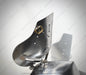 A close-up of a metallic armor plate or shield component with a polished steel finish, featuring pre-drilled holes and a small brass-colored hardware detail, set against a light gray background with a prominent cast shadow.