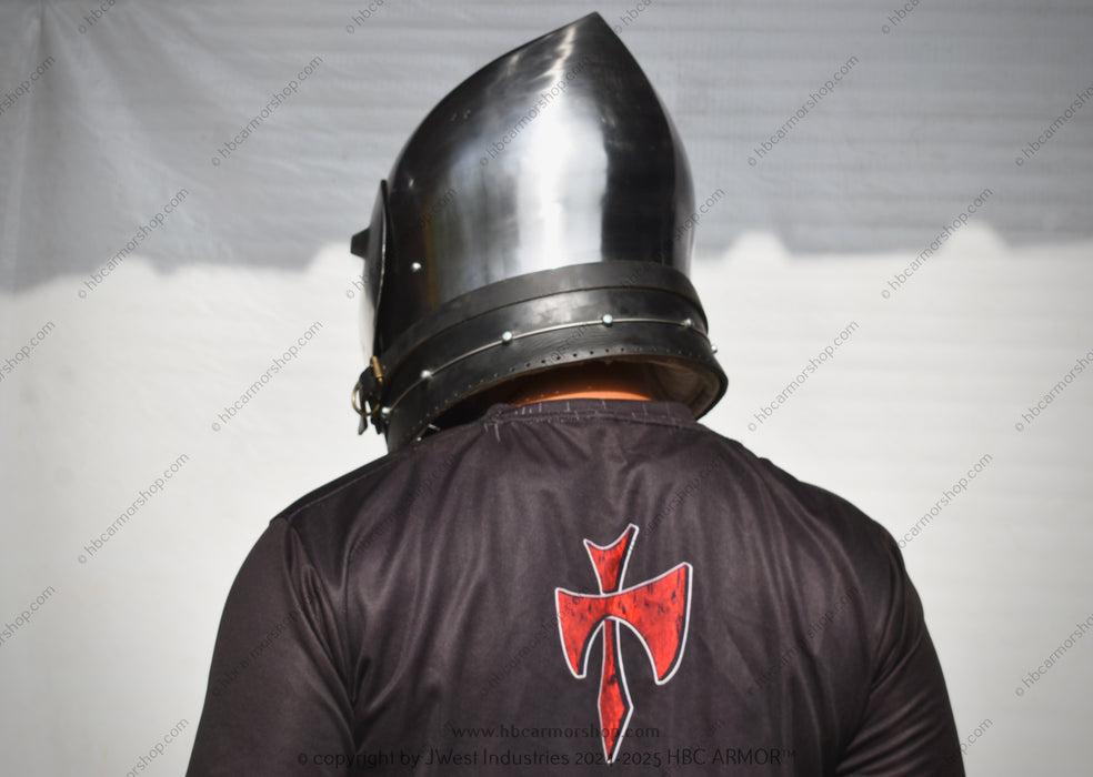 A person viewed from behind wearing a polished steel medieval-style helmet and a black tunic with a red Templar cross emblem on the back, set against a white draped backdrop.