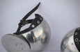 A close-up of a polished steel falcon helmet with a black leather chin strap and silver rivets, shown against a plain light background.