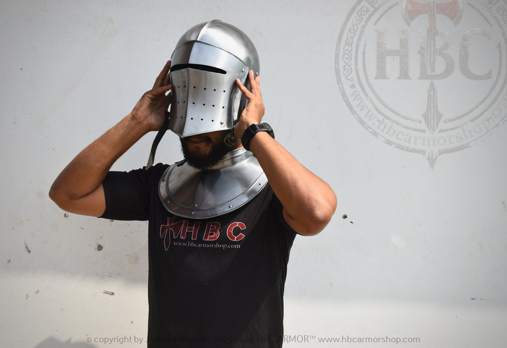 A man wearing a polished steel medieval knight helmet and matching steel neck guard, adjusting the helmet with both hands. He is wearing a black t-shirt with red and white 'HBC' branding.