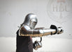 A person wearing full medieval-style steel plate armor with a helmet, breastplate, gauntlets, and a chainmail coif, posed against a plain light background. A faint HBC Armor logo watermark appears behind the subject.