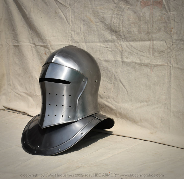 A polished steel medieval helmet with a visor and neck guard, displayed on a beige fabric backdrop.