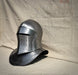 A polished steel medieval helmet with a visor and neck guard, displayed on a beige fabric backdrop.