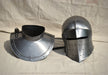 A medieval-style steel helmet and matching neck guard displayed side by side on a beige fabric backdrop.