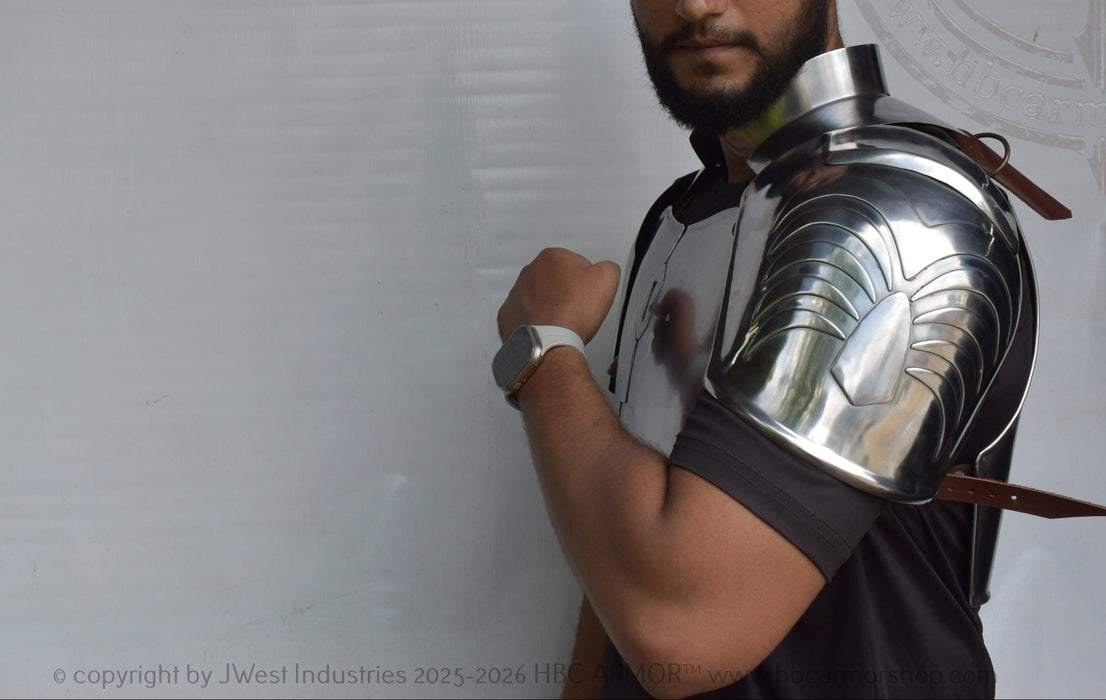 A man wearing a polished steel gladiator-style shoulder armor piece with a neck guard and leather straps, standing against a white backdrop.