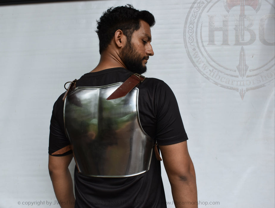 A man shown from the back wearing a metallic steel breastplate armor vest over a black t-shirt, standing in front of a white backdrop.