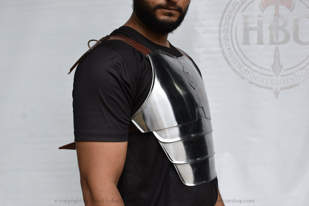 A man wearing a polished steel plate chest armor piece over a black t-shirt, shown from the chest up against a light gray background with a faint watermark.