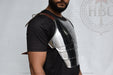 A man wearing a polished steel plate chest armor piece over a black t-shirt, shown from the chest up against a light gray background with a faint watermark.