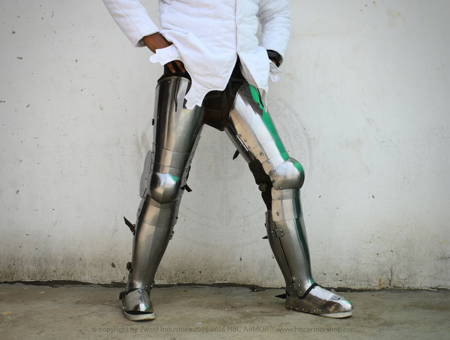 A person wearing metallic silver fantasy or costume leg armor with black and green accents, standing against a plain light wall.