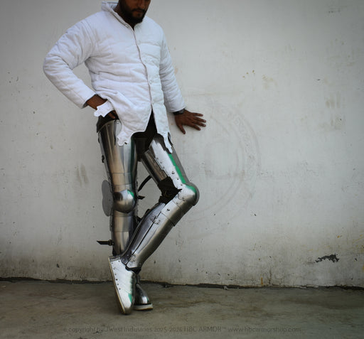 A man wearing a white puffer jacket and metallic chrome exoskeleton leg armor, standing against a plain concrete wall.