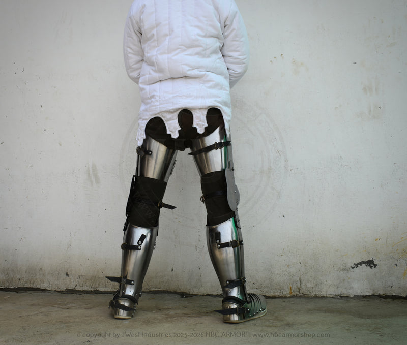 A person viewed from behind wearing a white quilted jacket and heavy metal leg armor with black straps, standing against a plain light wall.