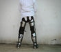 A person viewed from behind wearing a white quilted jacket and heavy metal leg armor with black straps, standing against a plain light wall.