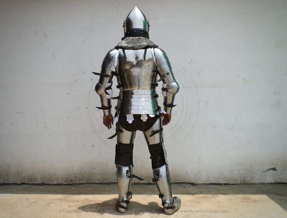 A full suit of medieval plate armor shown from the back, worn by a person standing against a plain off-white wall.