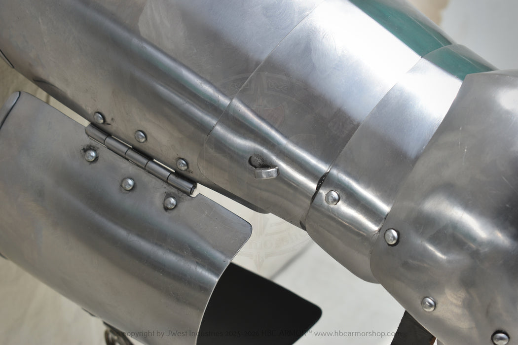 Close-up of a metallic armor plate or cannon plate with rivets and a hinge, showing a brushed silver steel finish.