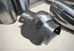 A dark metallic plate armor piece with a curved, multi-panel design, displayed on a light concrete floor alongside other steel armor components.